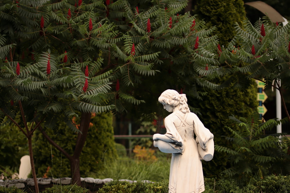 a statue of a woman holding a bird in a garden