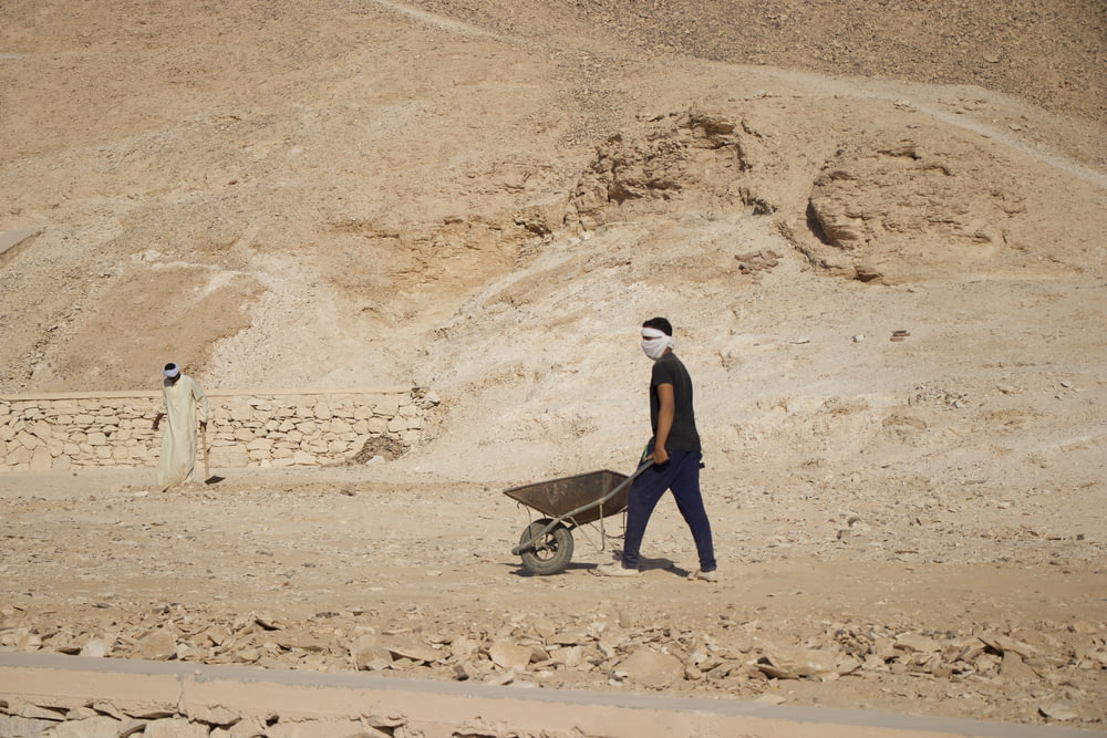 Un hombre caminando en el desierto con una carretilla