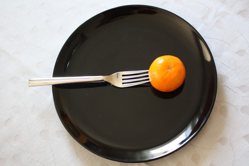 a black plate with a fork and an orange on it