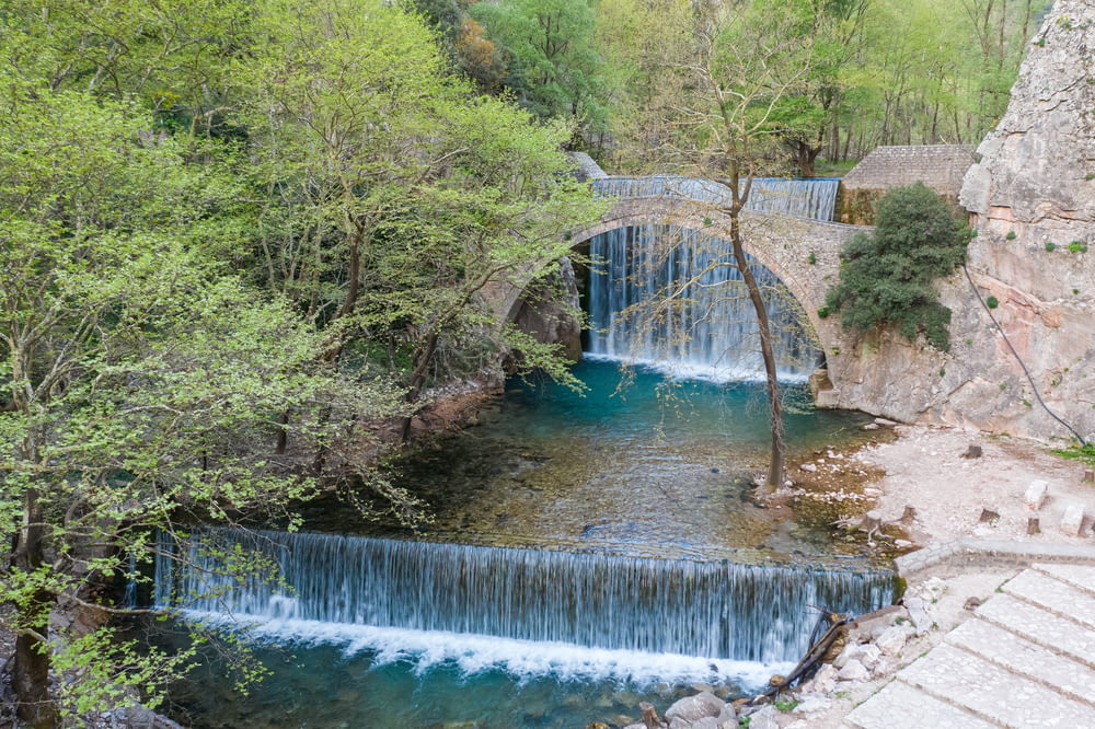 a waterfall flowing under a bridge next to a forest