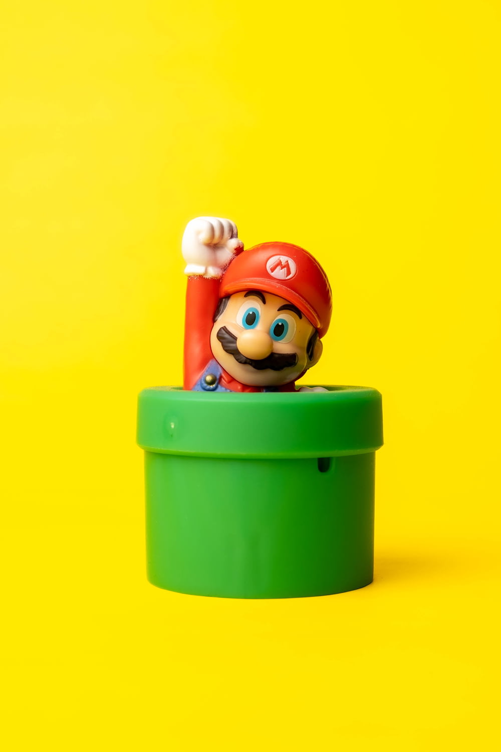 a toy mario in a green container on a yellow background