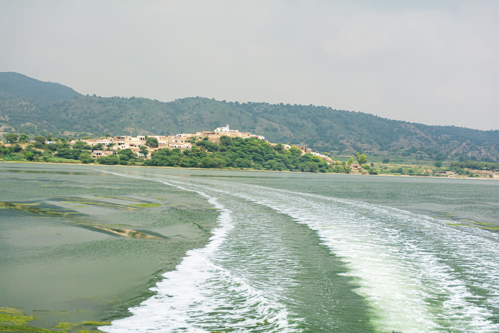 a boat traveling down a river next to a lush green hillside