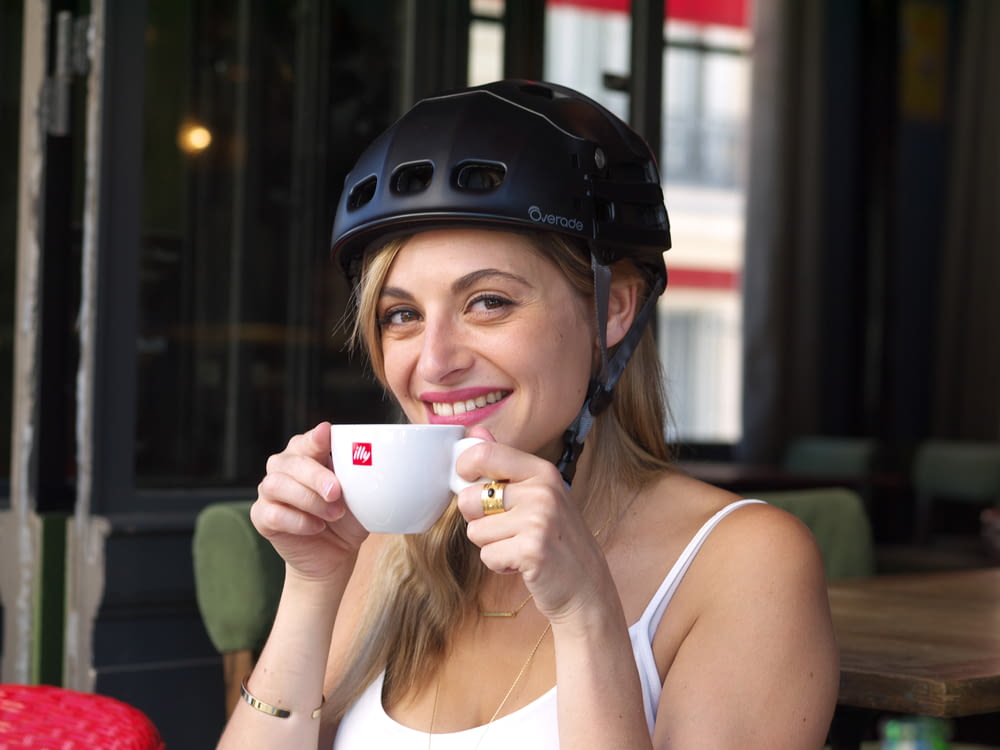 a woman wearing a helmet drinking a cup of coffee