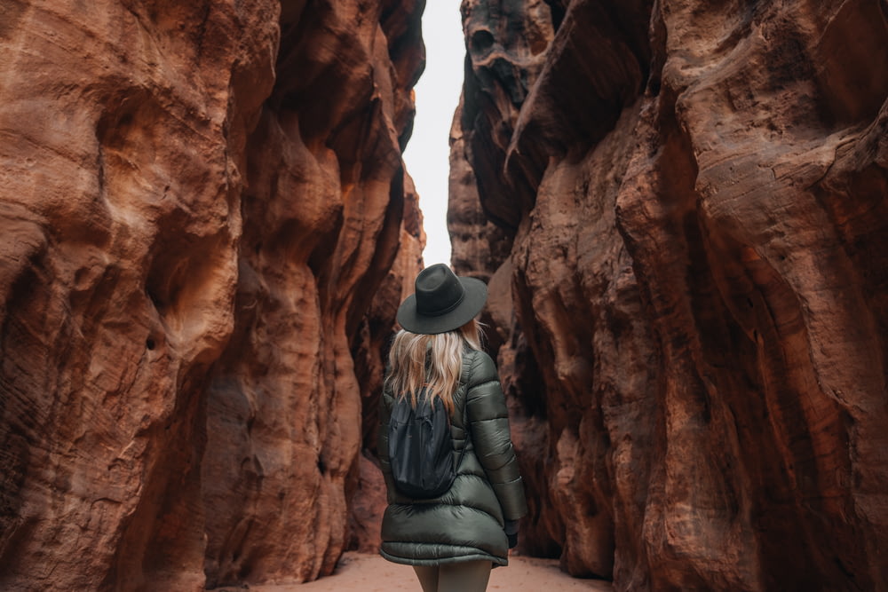a woman in a hat and coat walking through a canyon