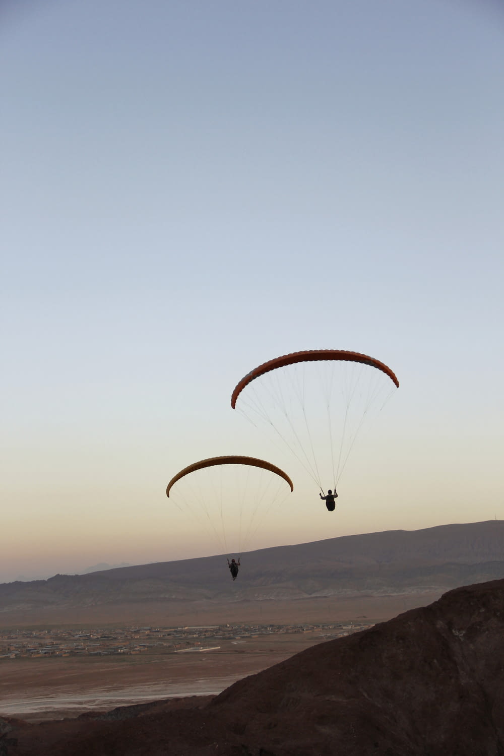 two parasailers in the air over a desert landscape