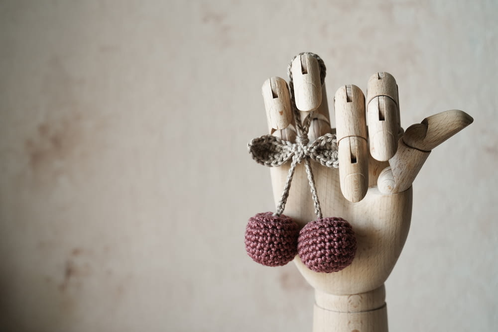 a wooden hand with two knitted balls hanging from it