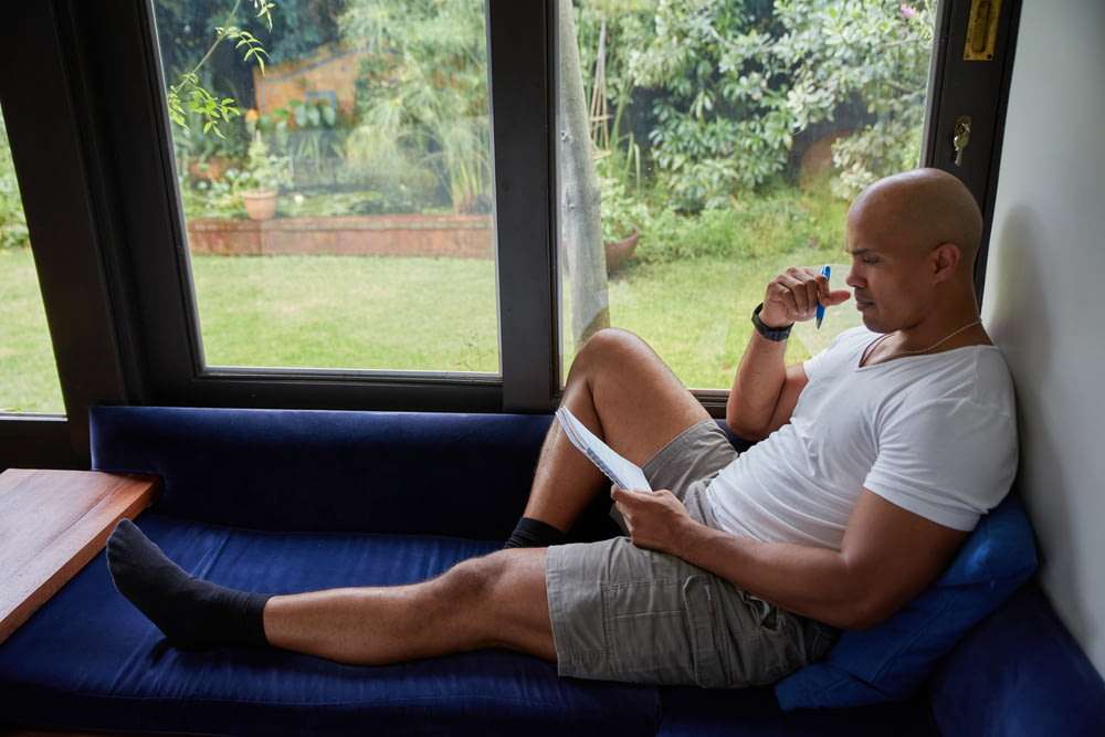 a man sitting on a blue couch looking out a window