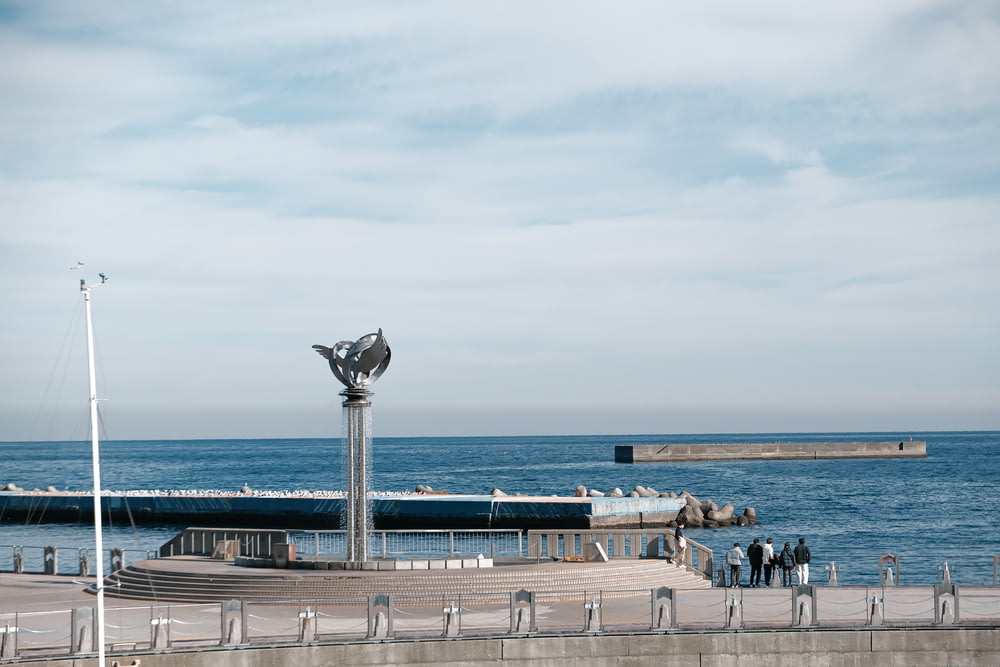 a statue of a bird on top of a pole next to a body of water