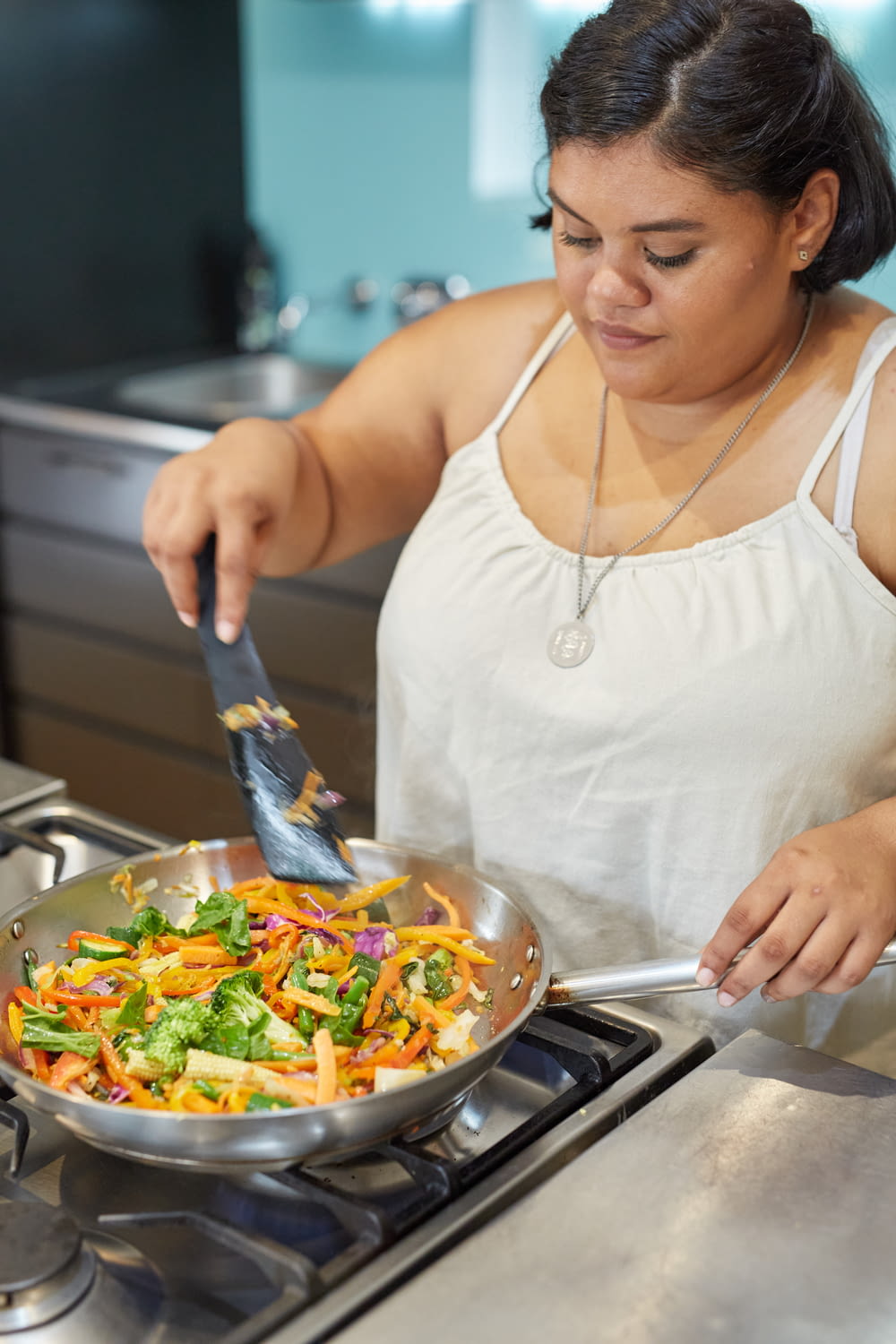 a woman in a white tank top is cooking vegetables