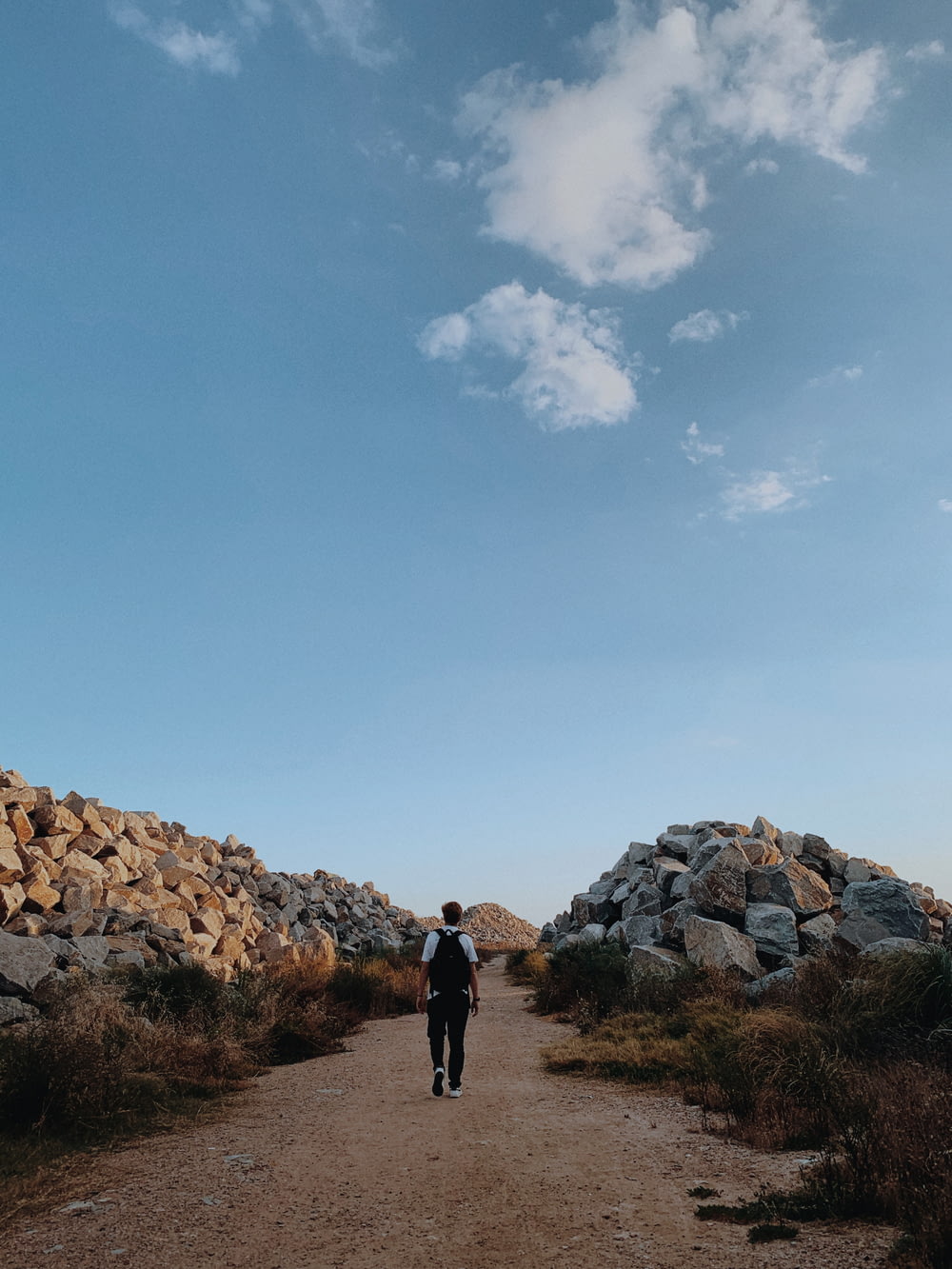 a man walking down a dirt road next to a pile of rocks