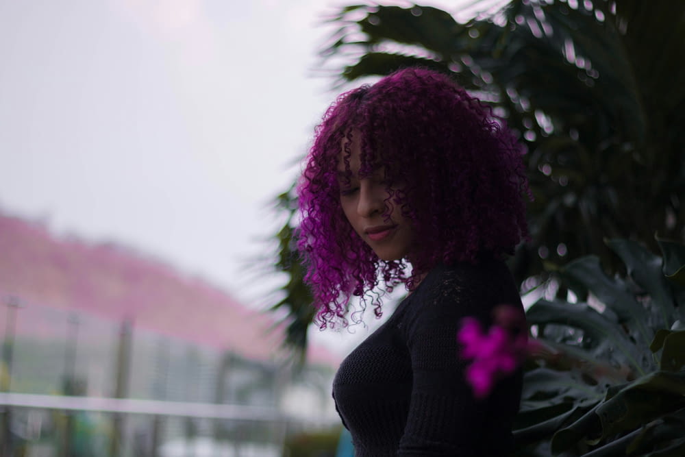 a woman with purple hair standing next to a plant