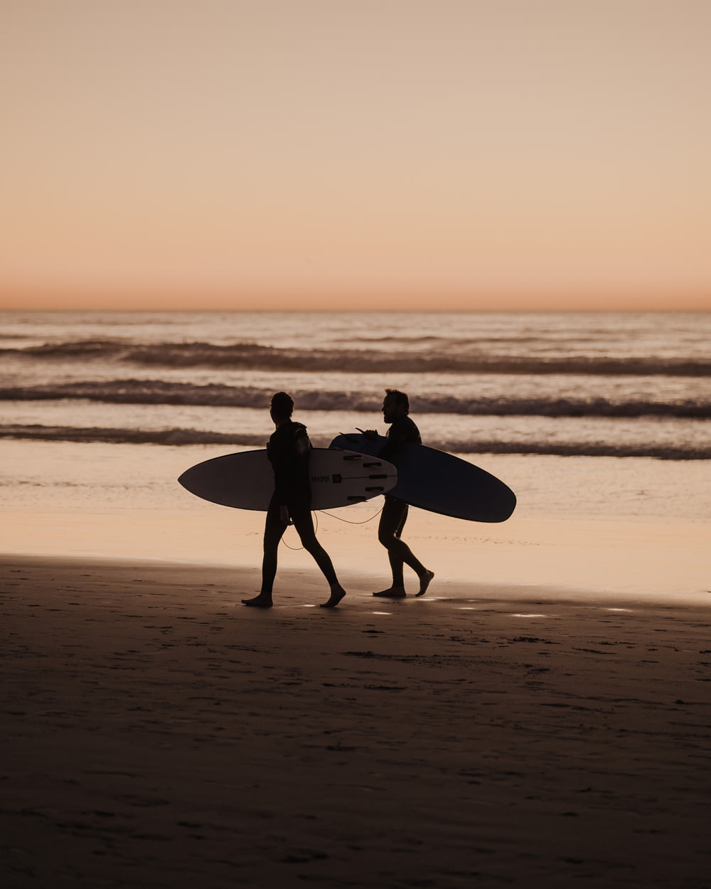 two people walking on a beach with a surfboard