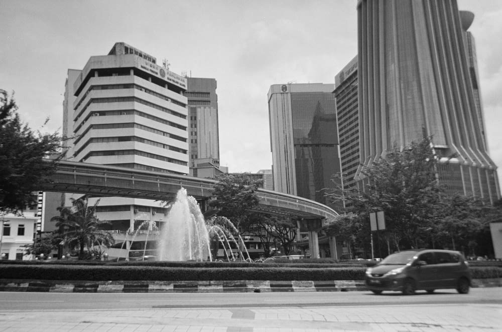 a black and white photo of a city with a fountain