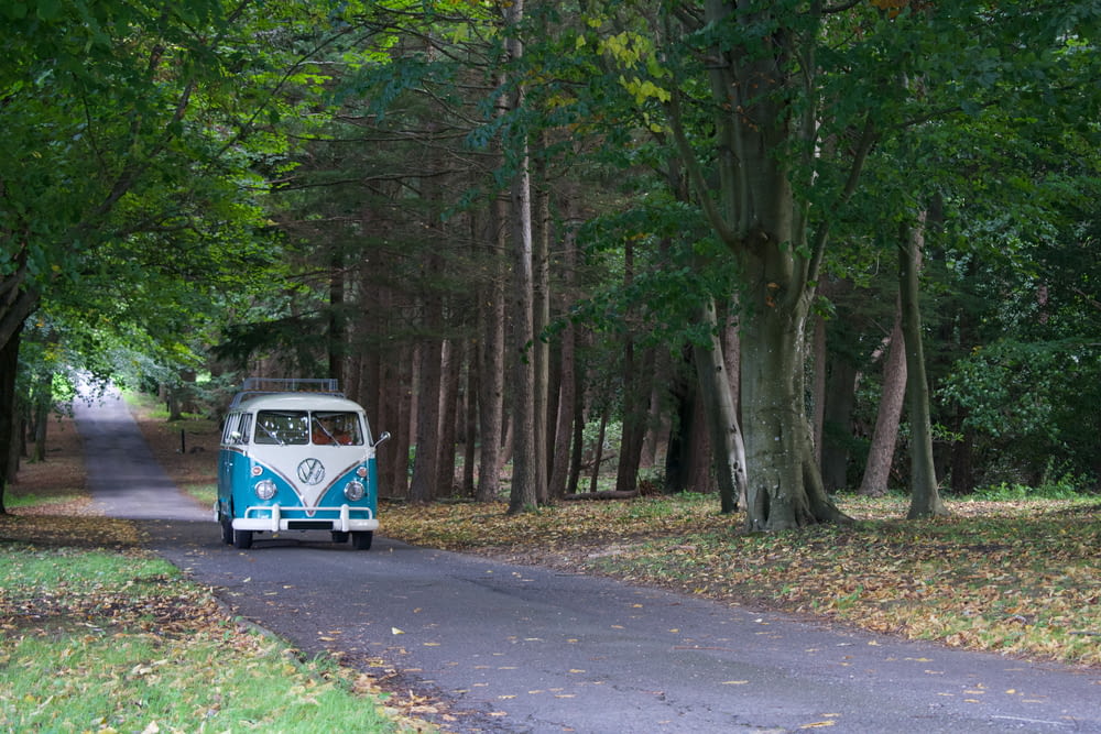 a blue and white bus driving down a tree lined road