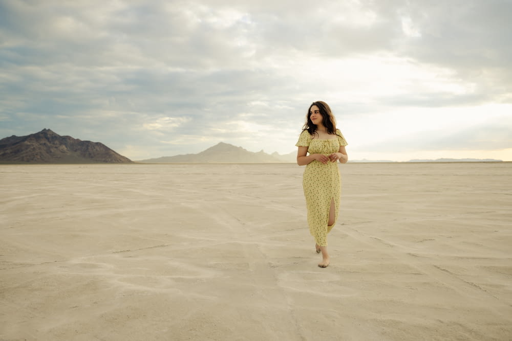 a woman in a yellow dress standing in the middle of a desert