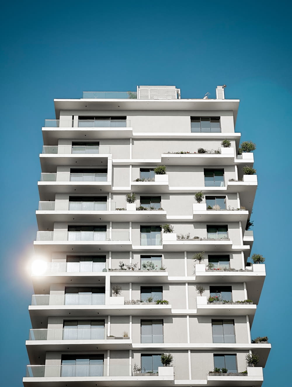 a tall white building with balconies and plants on the balconies