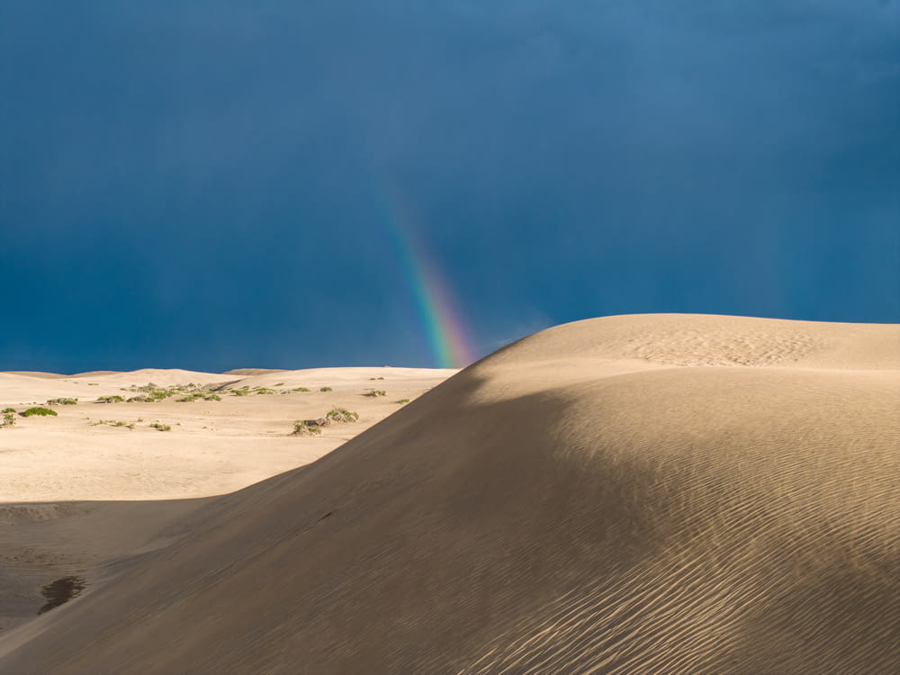 Un arc-en-ciel brille dans le ciel au-dessus d’une dune de sable