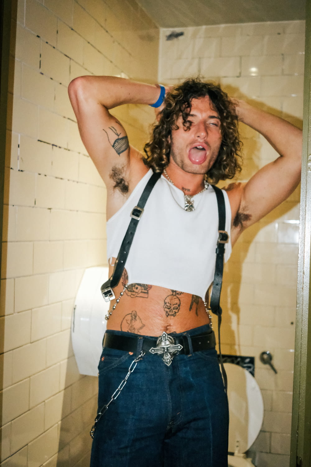 a man with long hair wearing suspenders in a bathroom