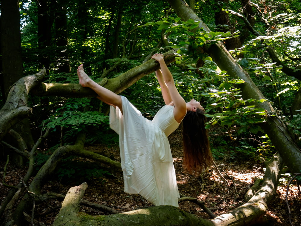 a woman in a white dress standing on a branch in the woods