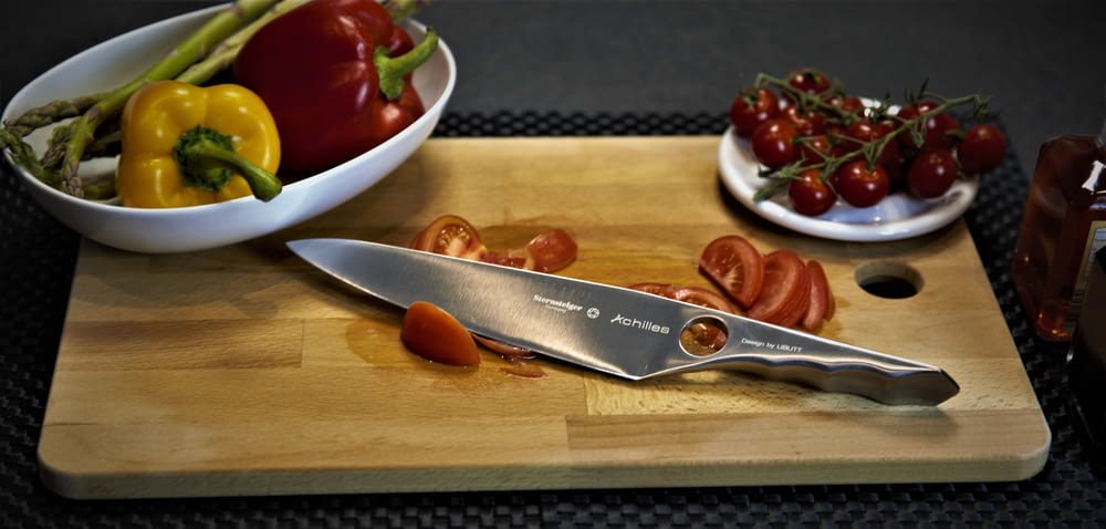 un tagliere sormontato da un coltello e una ciotola di verdure