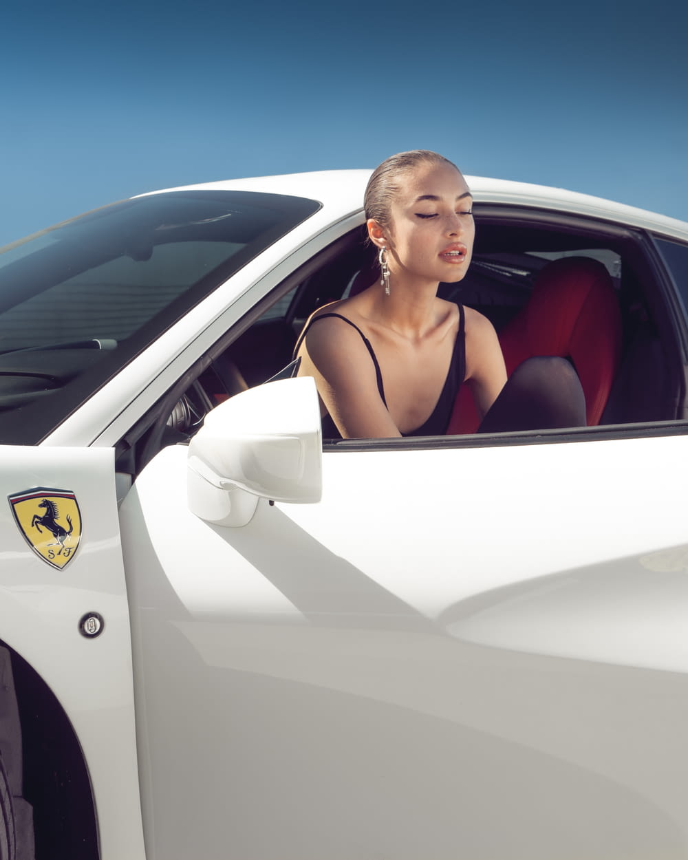 a woman sitting in the drivers seat of a white sports car