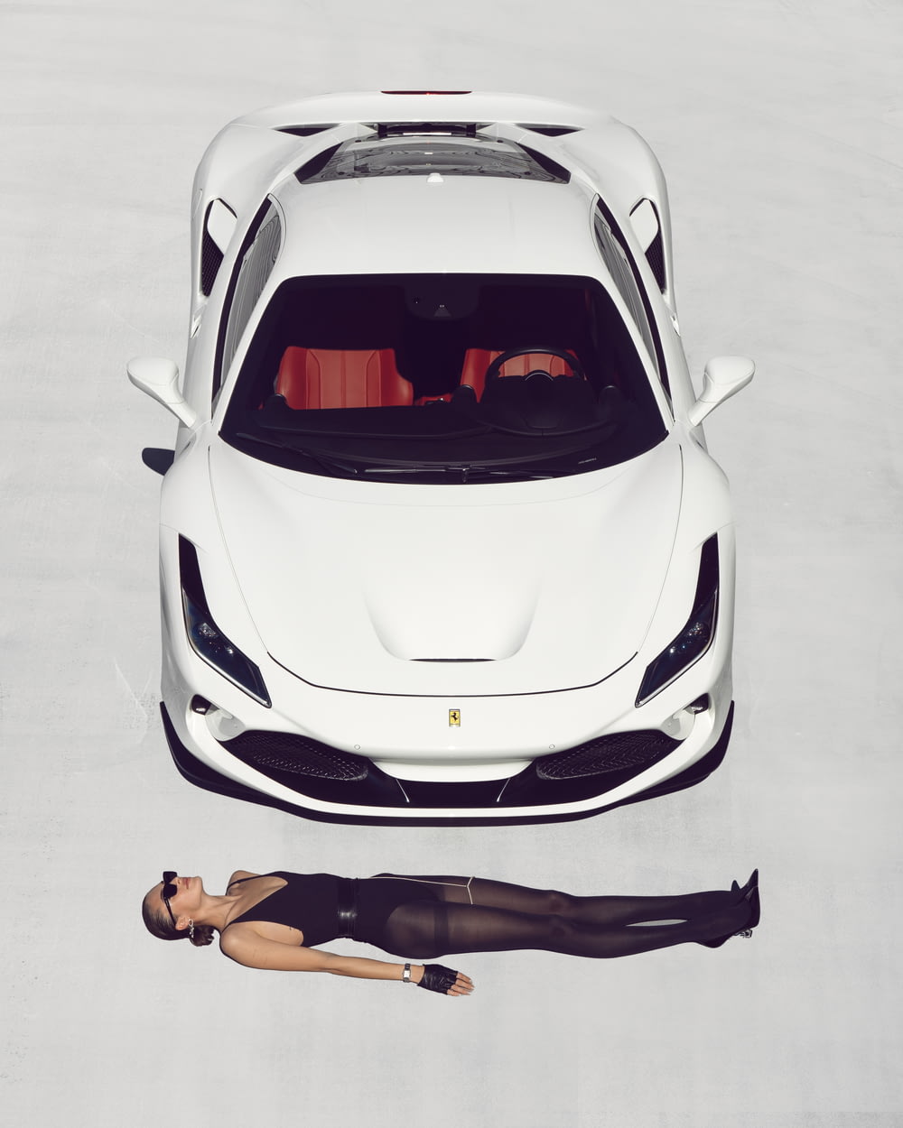 a woman laying on the ground next to a white sports car