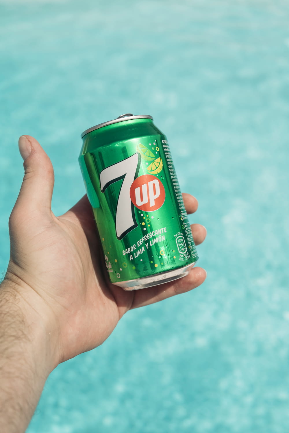 a hand holding a can of 7up by a pool