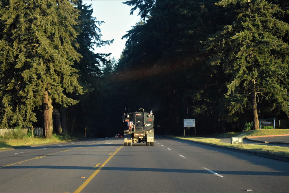 a truck driving down a road next to tall trees