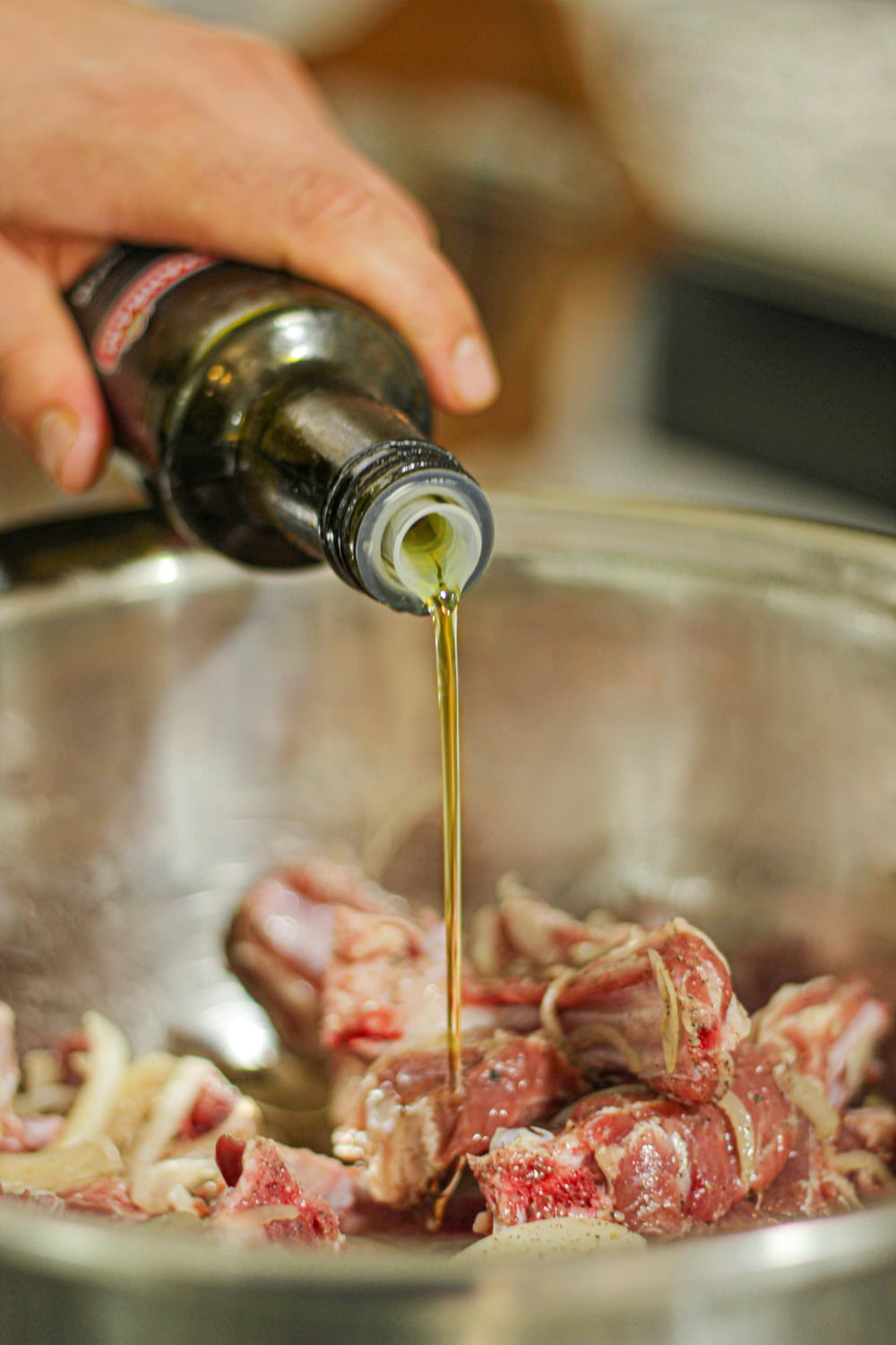 a person pouring olive into a pot filled with meat