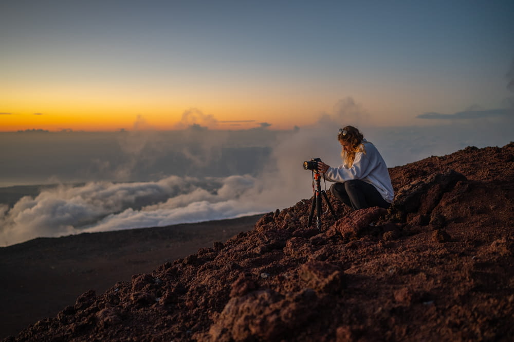 a woman sitting on top of a mountain with a camera