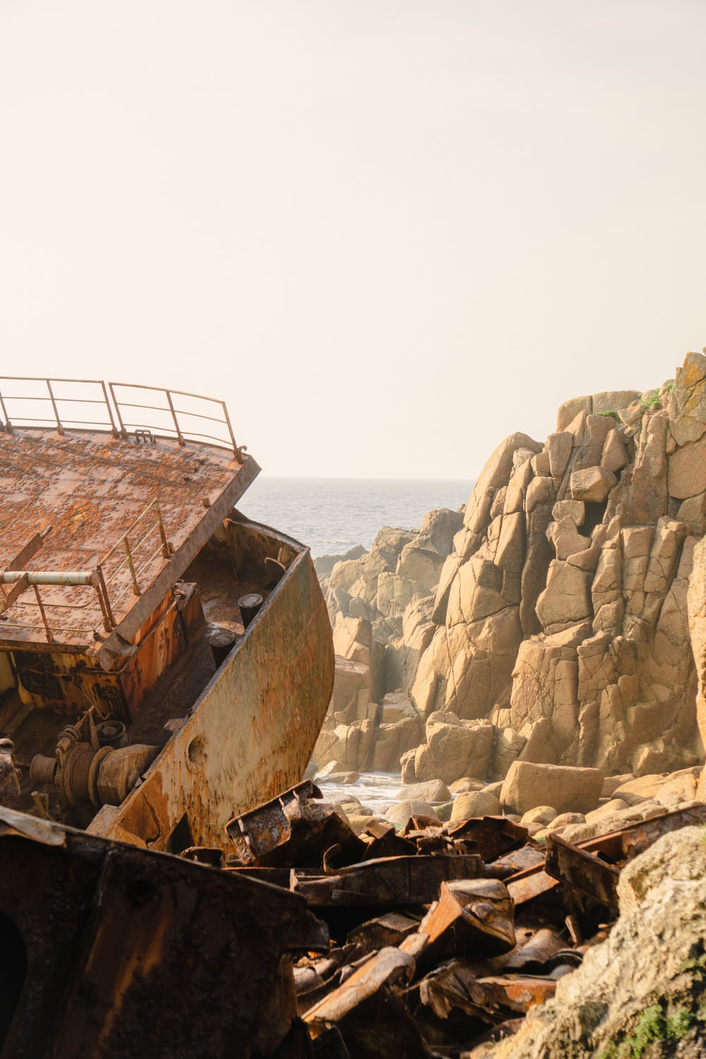 a rusted out boat sitting on top of a rocky beach