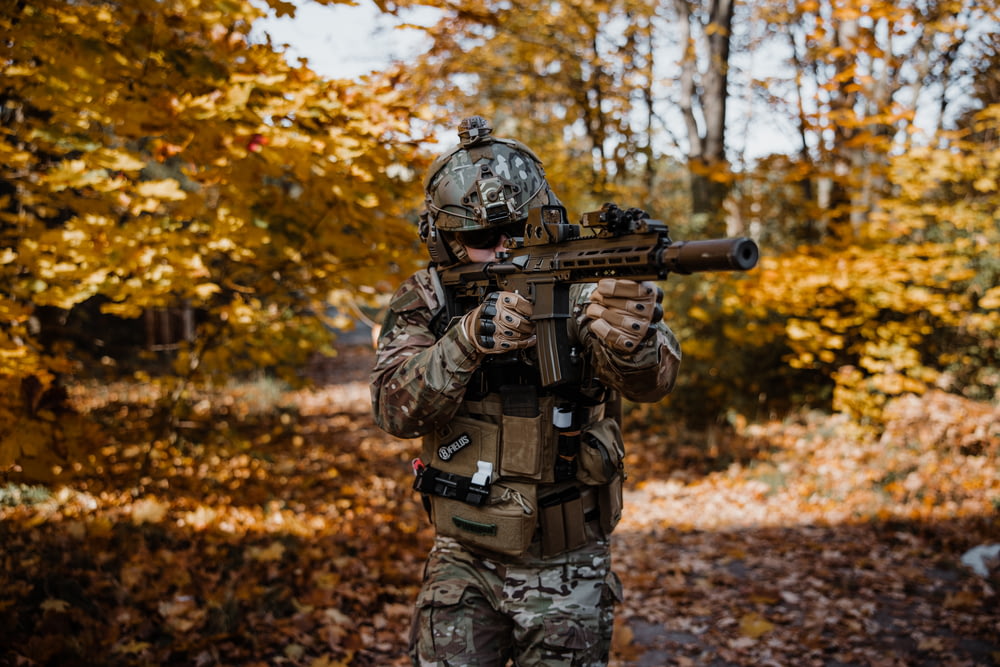 a man in camouflage holding a rifle in a wooded area