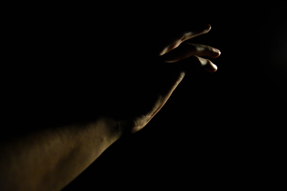 a hand reaching for a light bulb in the dark