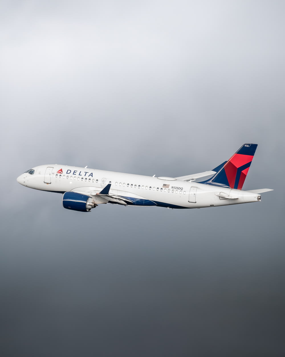 a delta airplane flying in a cloudy sky