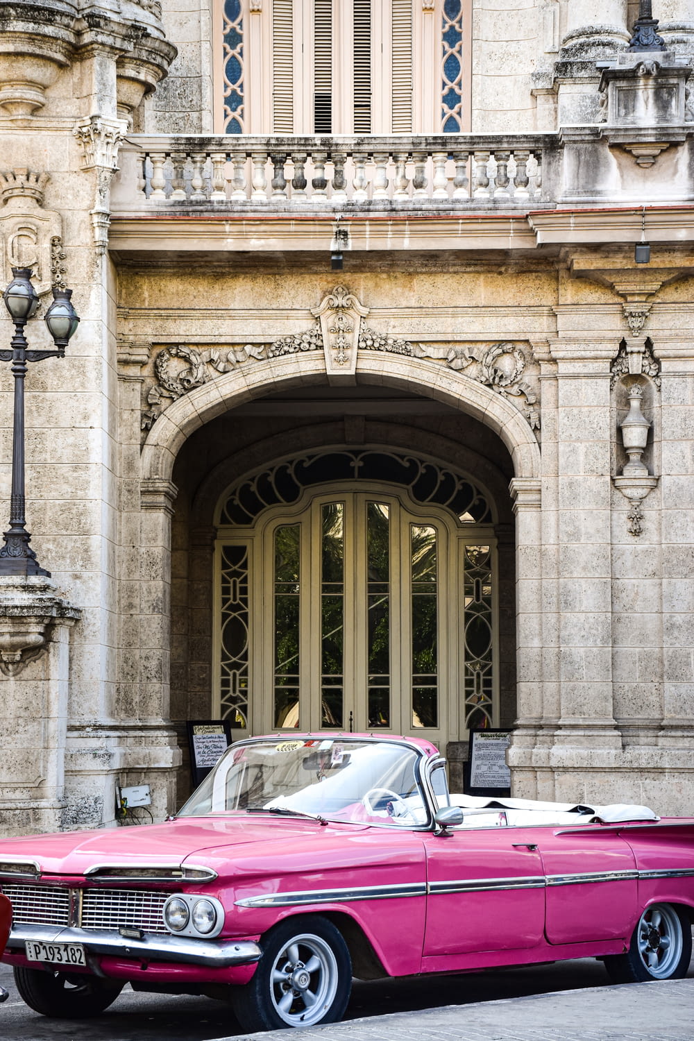 a pink classic car parked in front of a building