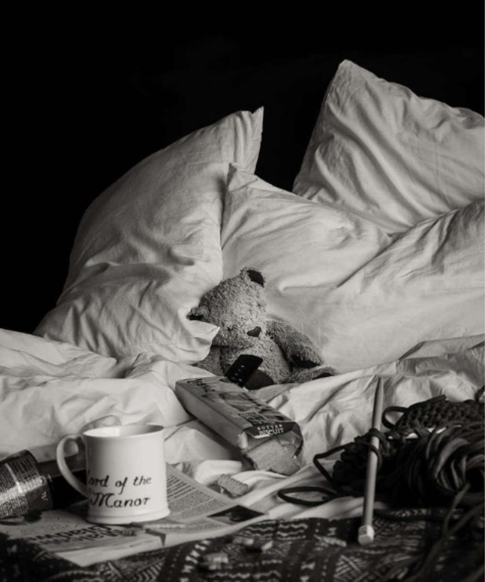 a teddy bear sitting on top of a bed next to a cup of coffee