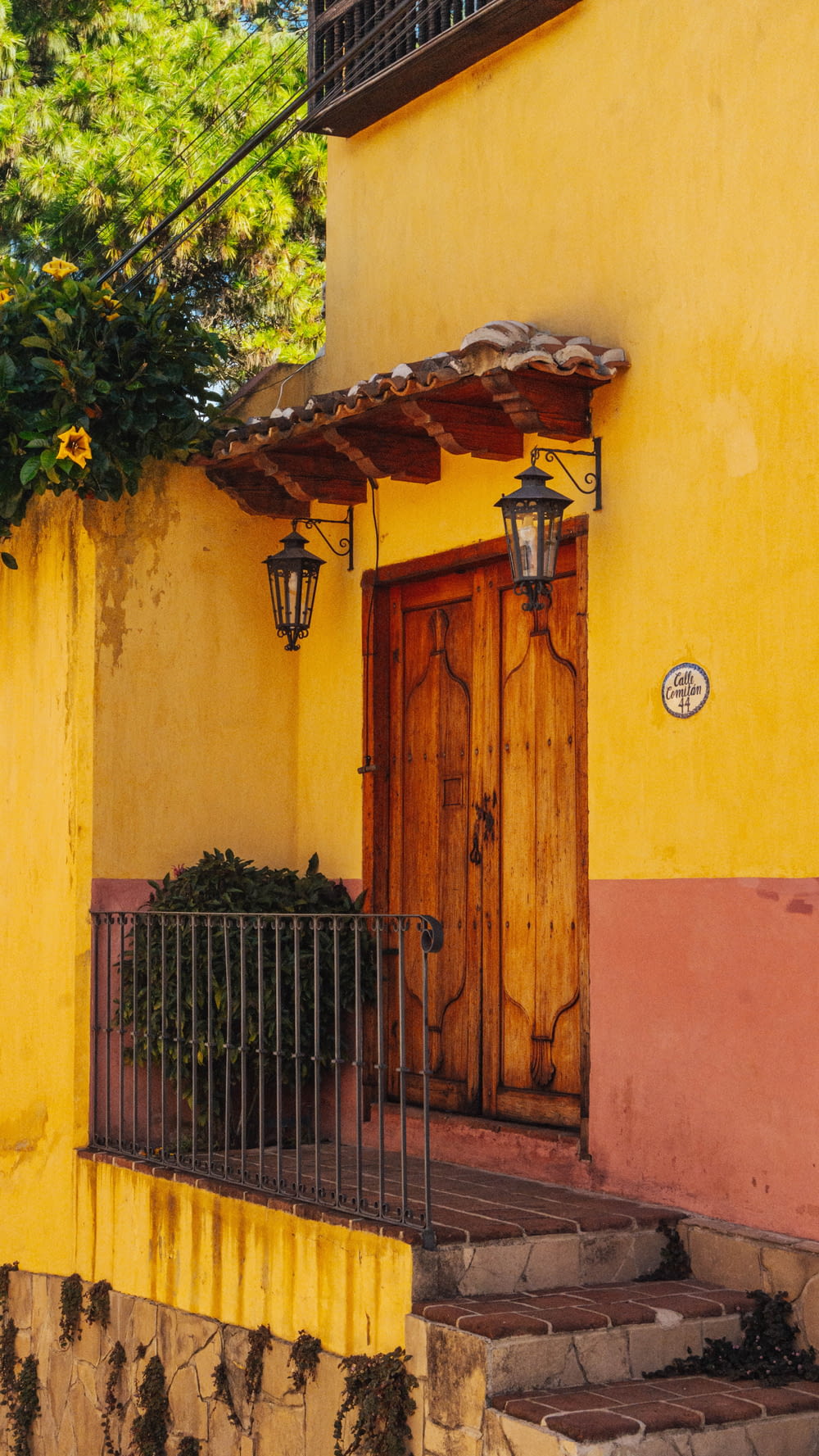 a yellow building with a wooden door and a wrought iron fence