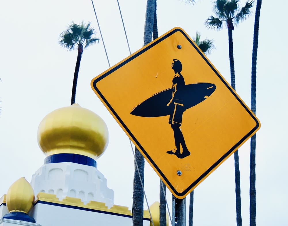 a yellow street sign with a picture of a person holding a surfboard