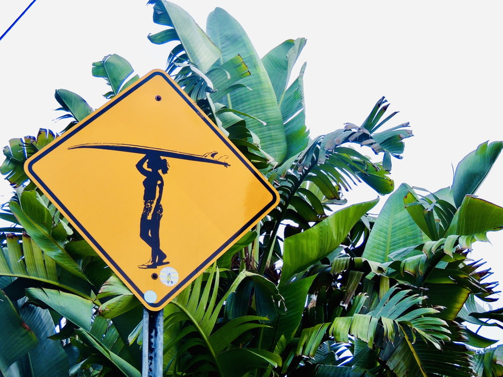 a yellow street sign with a man holding a surfboard on his head