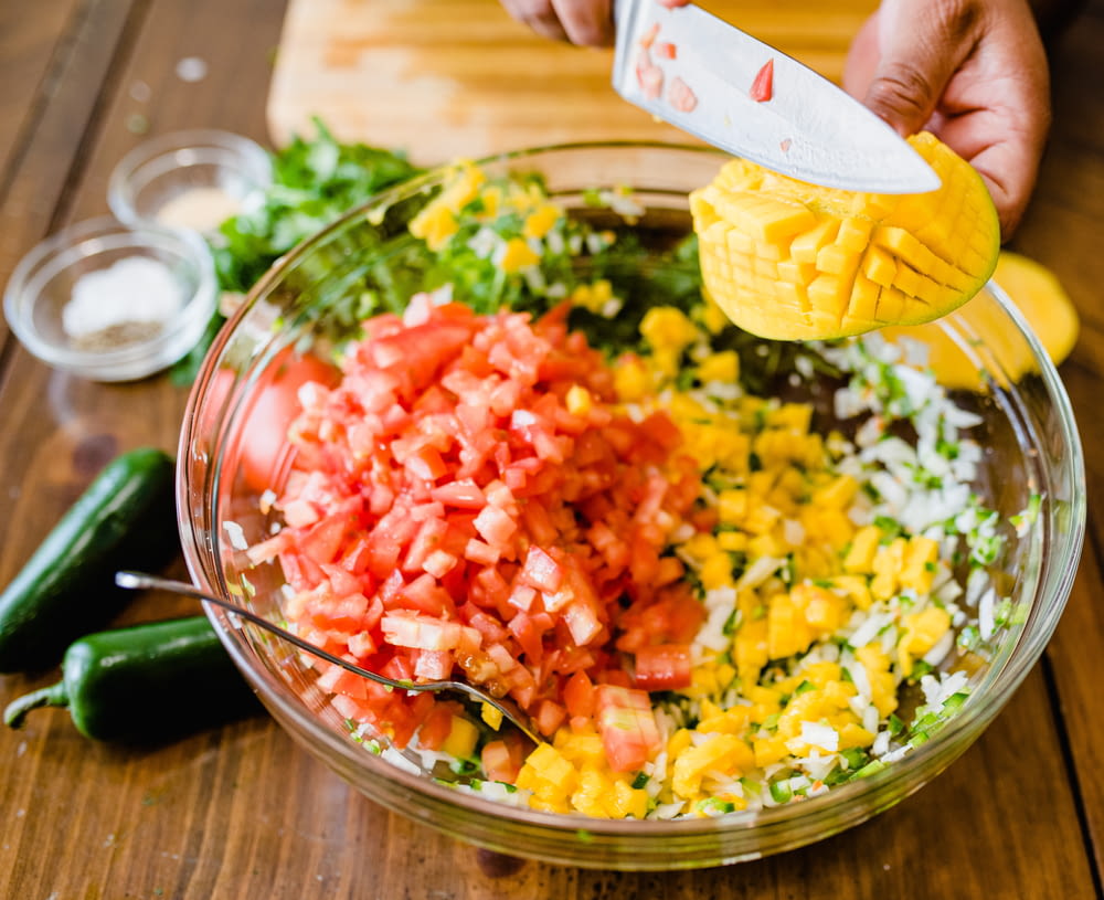 a person grating tomatoes, onions, and other vegetables into a bowl