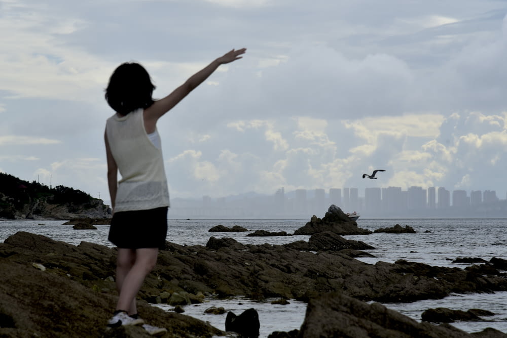 a woman standing on top of a rocky beach next to the ocean