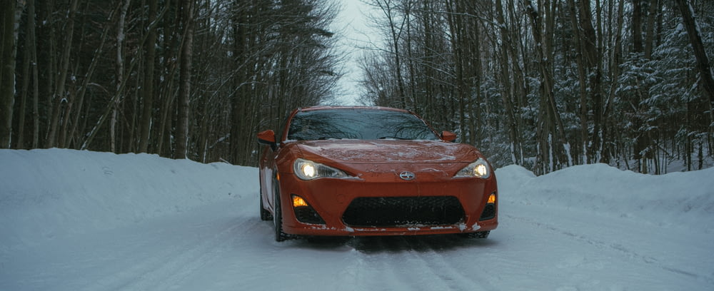 a red sports car driving down a snow covered road