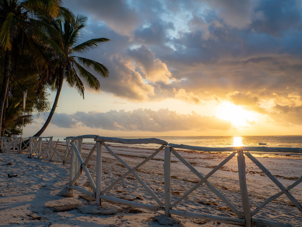 the sun is setting over the beach with palm trees