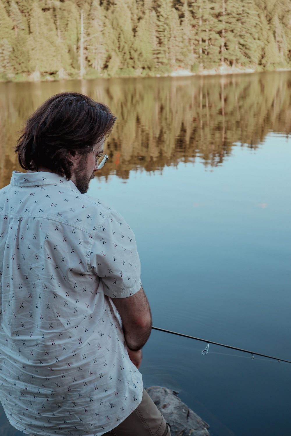 um homem pescando em um lago com árvores ao fundo