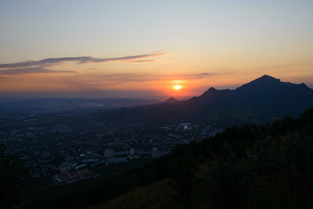 the sun is setting over a city and mountains