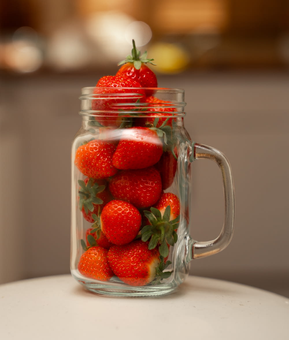 a glass jar filled with strawberries on top of a table