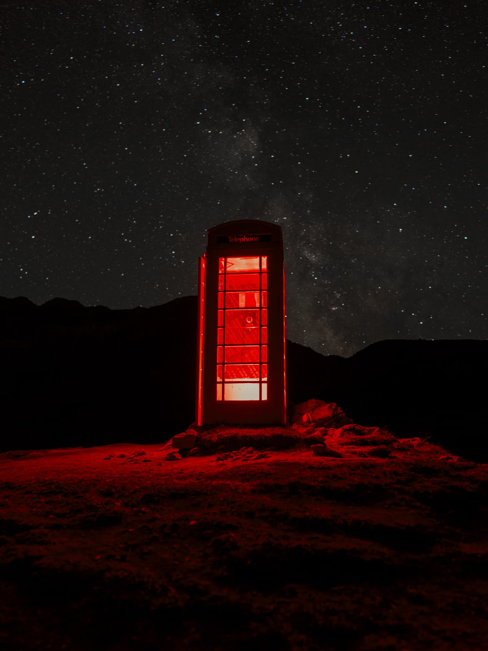 a red phone booth sitting on top of a hill under a night sky