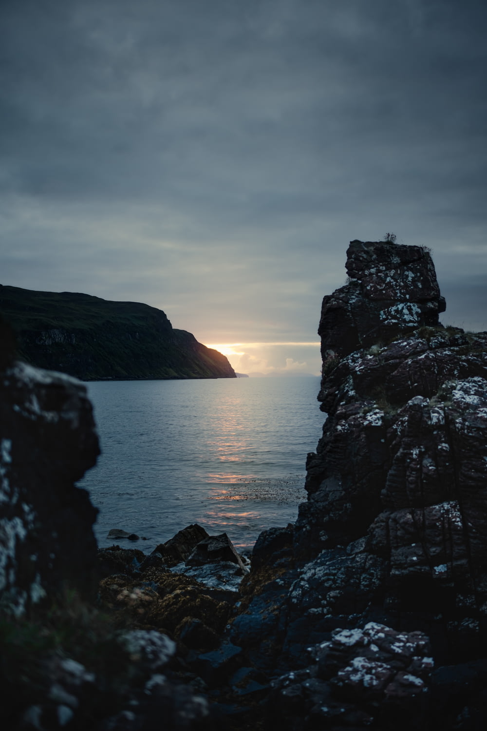the sun is setting over the water from a rocky cliff