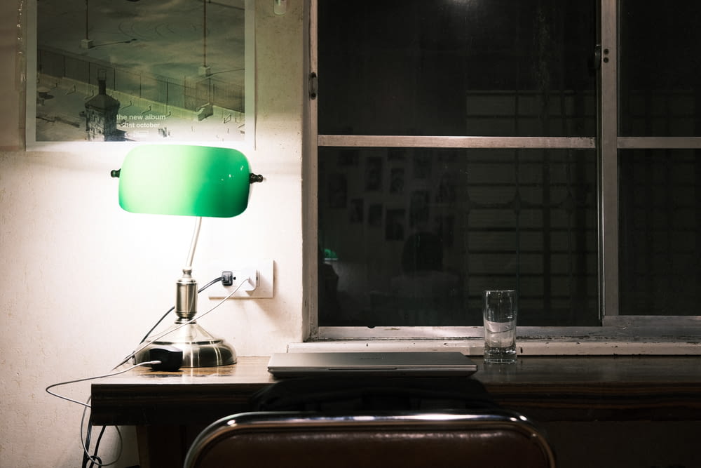 a green lamp sitting on top of a table next to a window