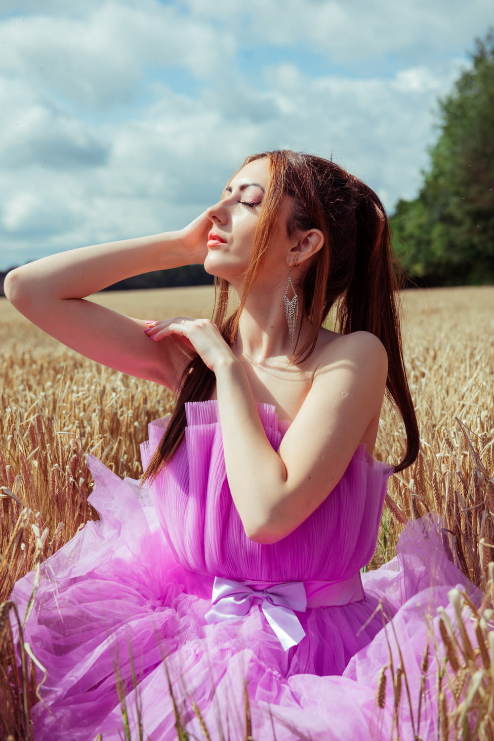 a woman in a pink dress sitting in a wheat field